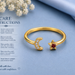 Gold adjustable ring with a crescent moon and star charm, one adorned with small clear stones and the other with a red gemstone, shown on a blue background with care instructions text.